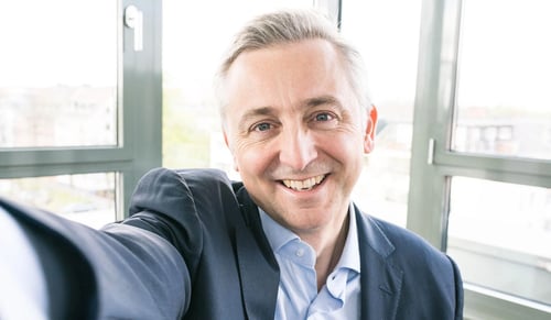 Jean-Marc Noel, CEO van Trusted Shops, lacht naar de camera en maakt een selfie in zijn kantoor.