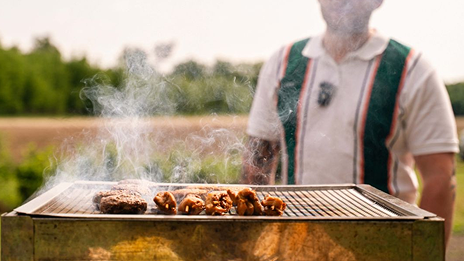 Een foto van een onherkenbaar iemand die in een weiland aan het barbecueën is.