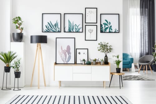 Botanische posters aan de muur in een woonkamerinterieur met witte kast, houten lamp en planten.